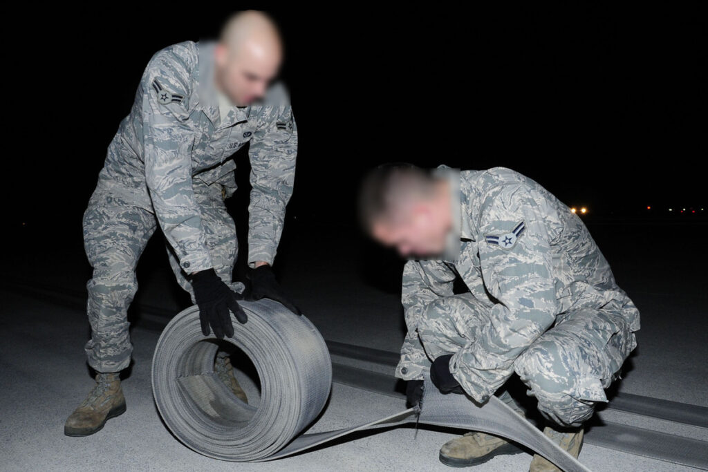 U.S. Air Force Airman 1st Class Curtis Woodward rolls up the old aircraft arresting tape while Airman 1st Class Justin Clifford cuts off the excess portion during the replacement of the aircraft arresting tape on Kadena Air Base, Japan Dec. 6, 2013. Cutting the old tape allows the barrier maintenance Airmen to roll the tape into groups and easily remove it from the flight line. Woodward is assigned to the 18th Civil Engineer Squadron electrical power productiontechnician and hails from Vallejo, Calif and Clifford is assigned to the 18th Civil Engineer Squadron electrical power production technician from Wash. (U.S. Air Force photo by Staff Sgt. Darnell T. Cannady)